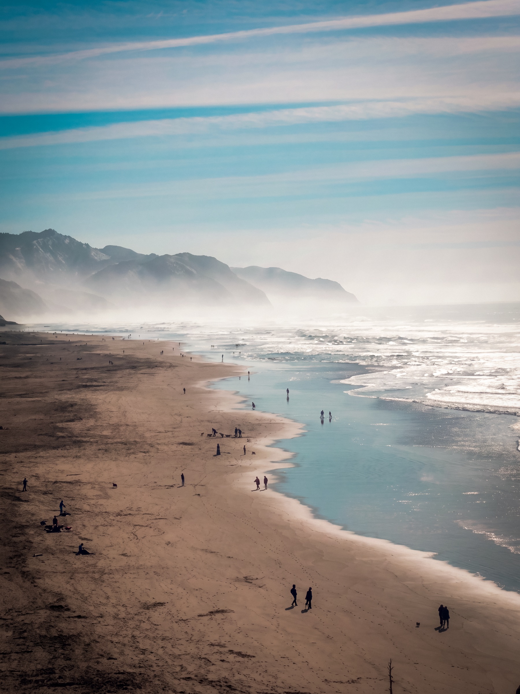 Ocean beach with misty mountains and people along the shoreline