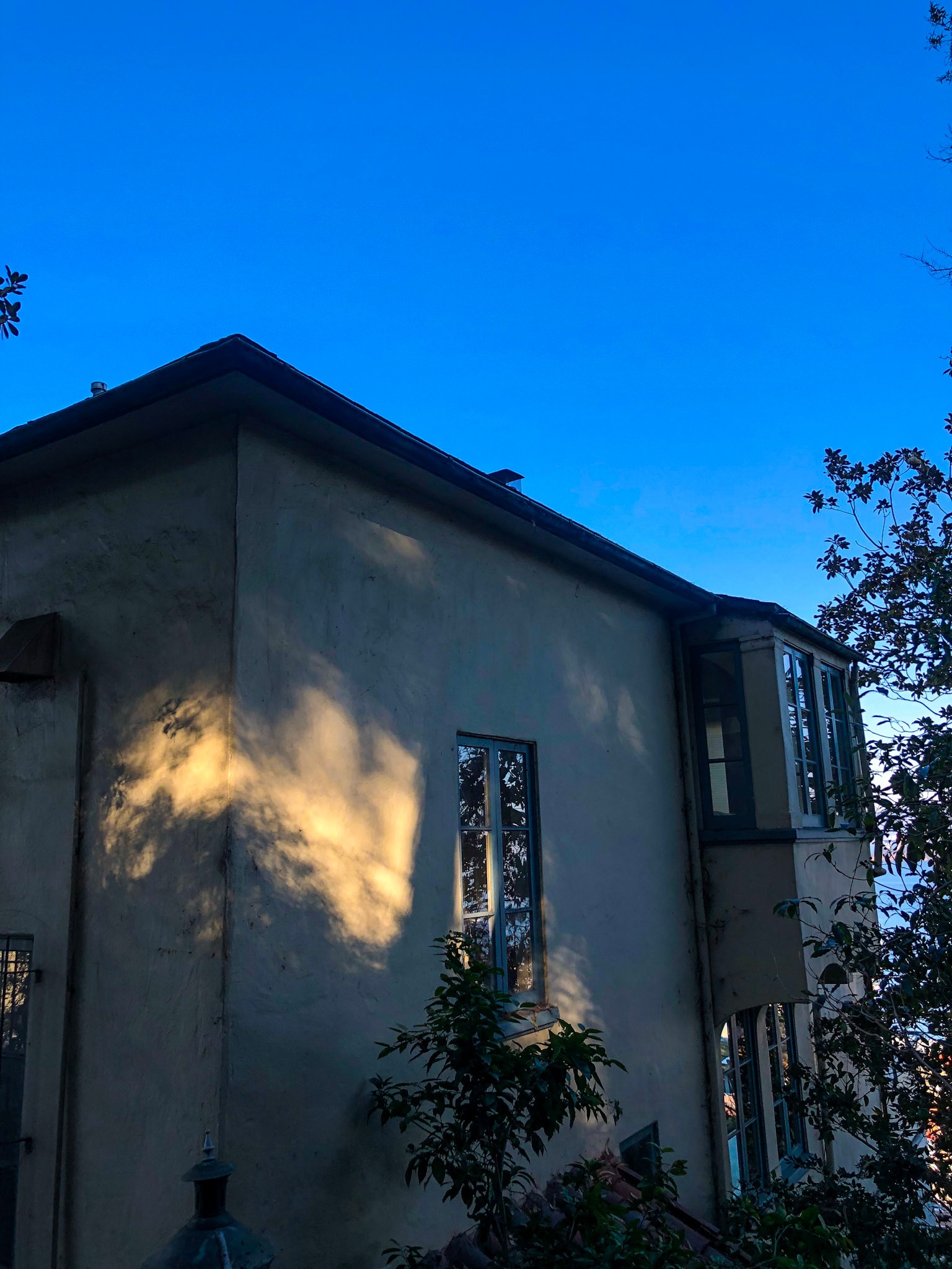 Sunlight and tree shadows across a house beneath a vivid blue sky