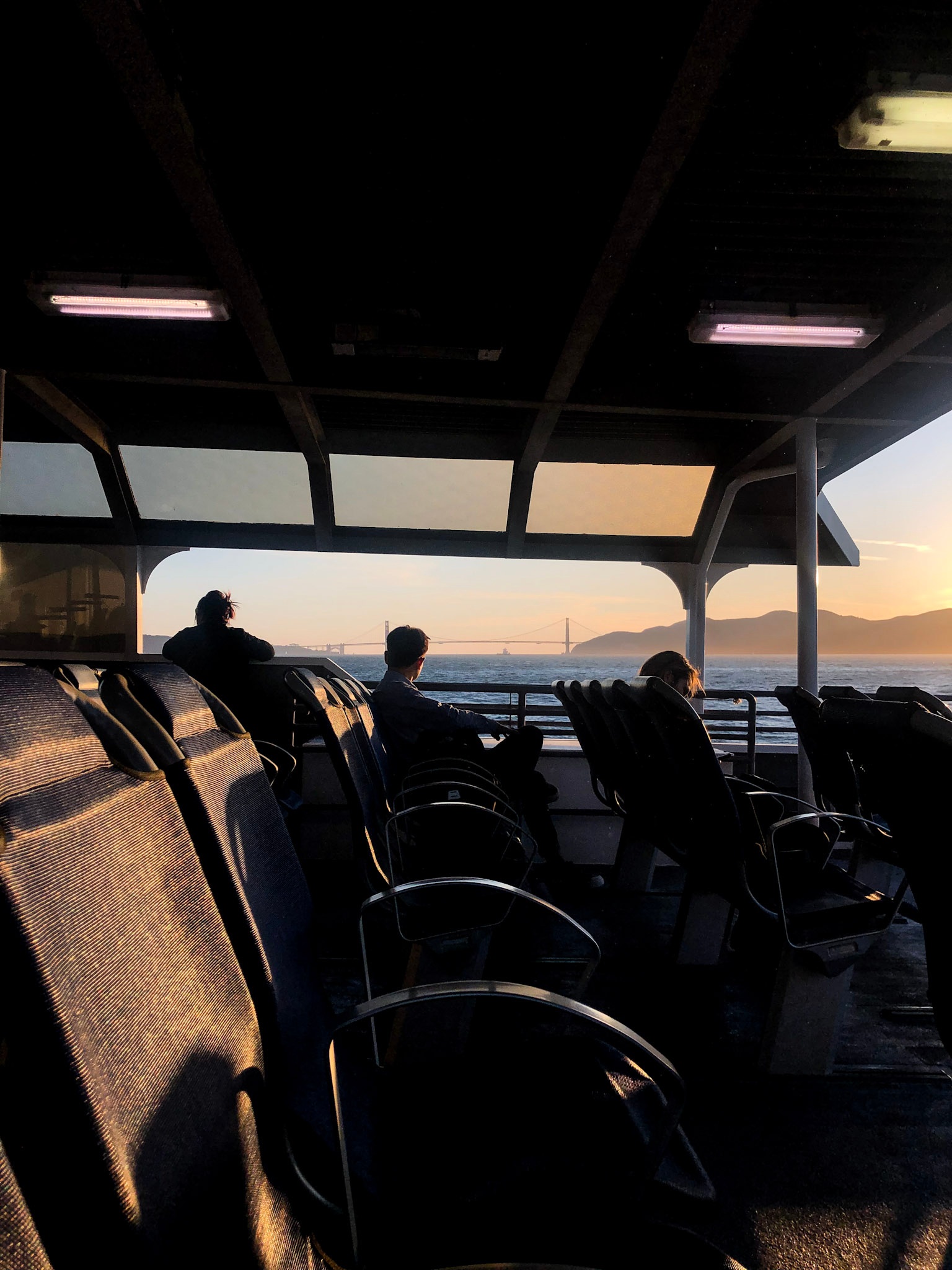 Passengers on a ferry at sunset with the Golden Gate Bridge across the bay