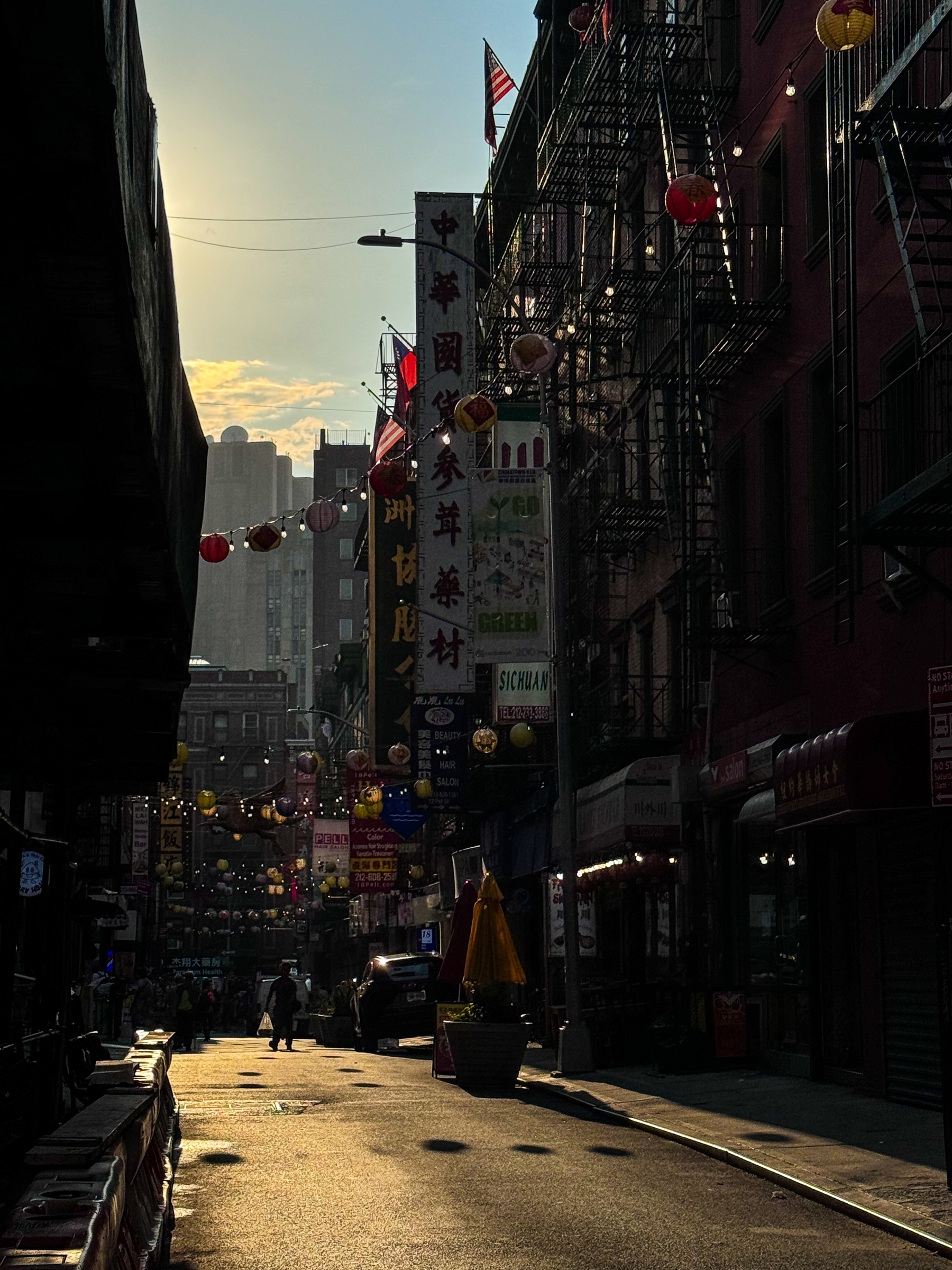 Lanterns and fire escapes above a city street in warm evening light